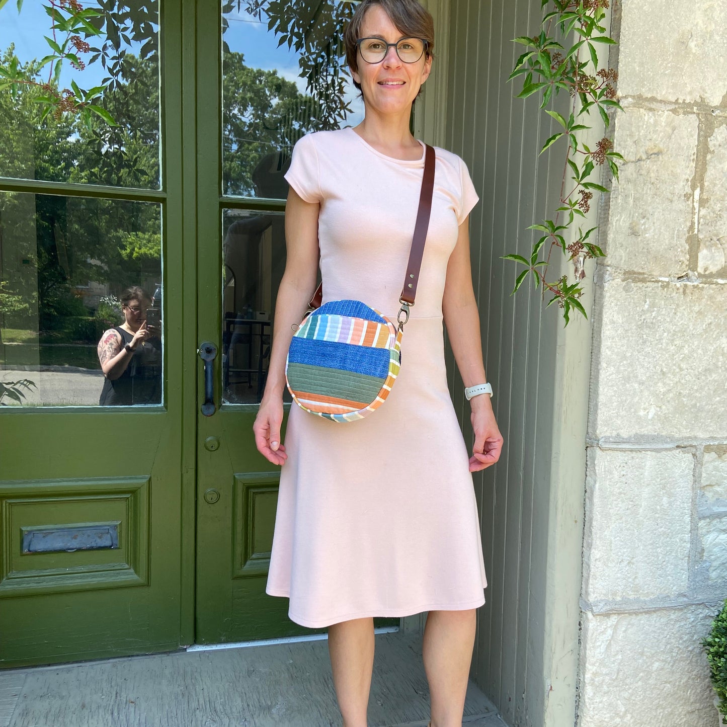 Woman holding a colorful bag in front of a green door